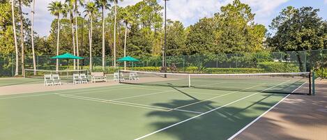 An outdoor tennis court with a net, benches, and umbrellas.