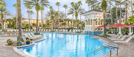 A swimming pool with lounge chairs and palm trees, surrounded by a building with a tiled facade.