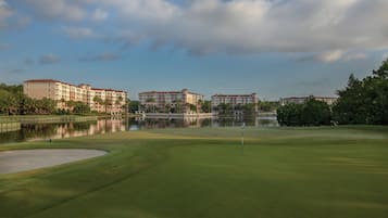 A golf course with a water body in the background, surrounded by buildings.