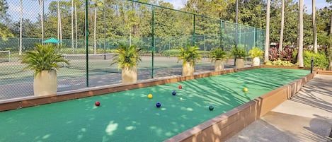 Un terrain de croquet doté d’une surface de jeu verte, entouré d’une clôture verte et de palmiers.