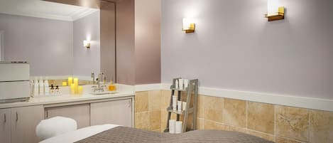 A hotel room with a bed, a vanity with toiletries, a mirror, and two wall-mounted lights.