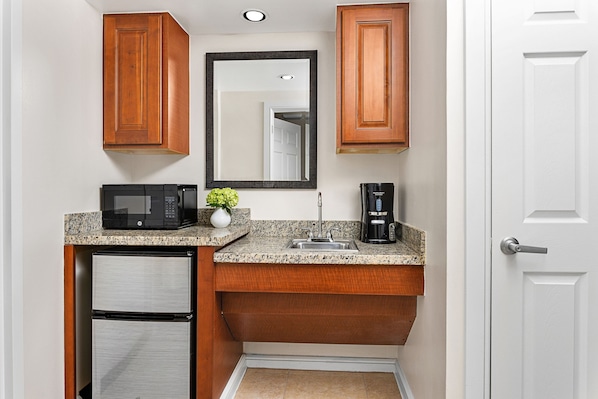A compact kitchen with wooden cabinets, a microwave, a coffee maker, and a refrigerator. - Marriott's Grande Vista (Orlando)