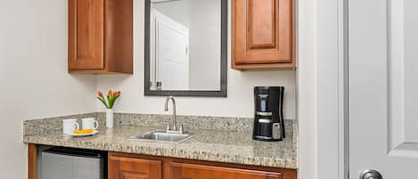 A kitchen with wooden cabinets, a granite countertop, a stainless steel refrigerator, a coffee maker, and a mirror.