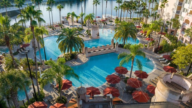 A resort pool area with palm trees, lounge chairs, and umbrellas.
