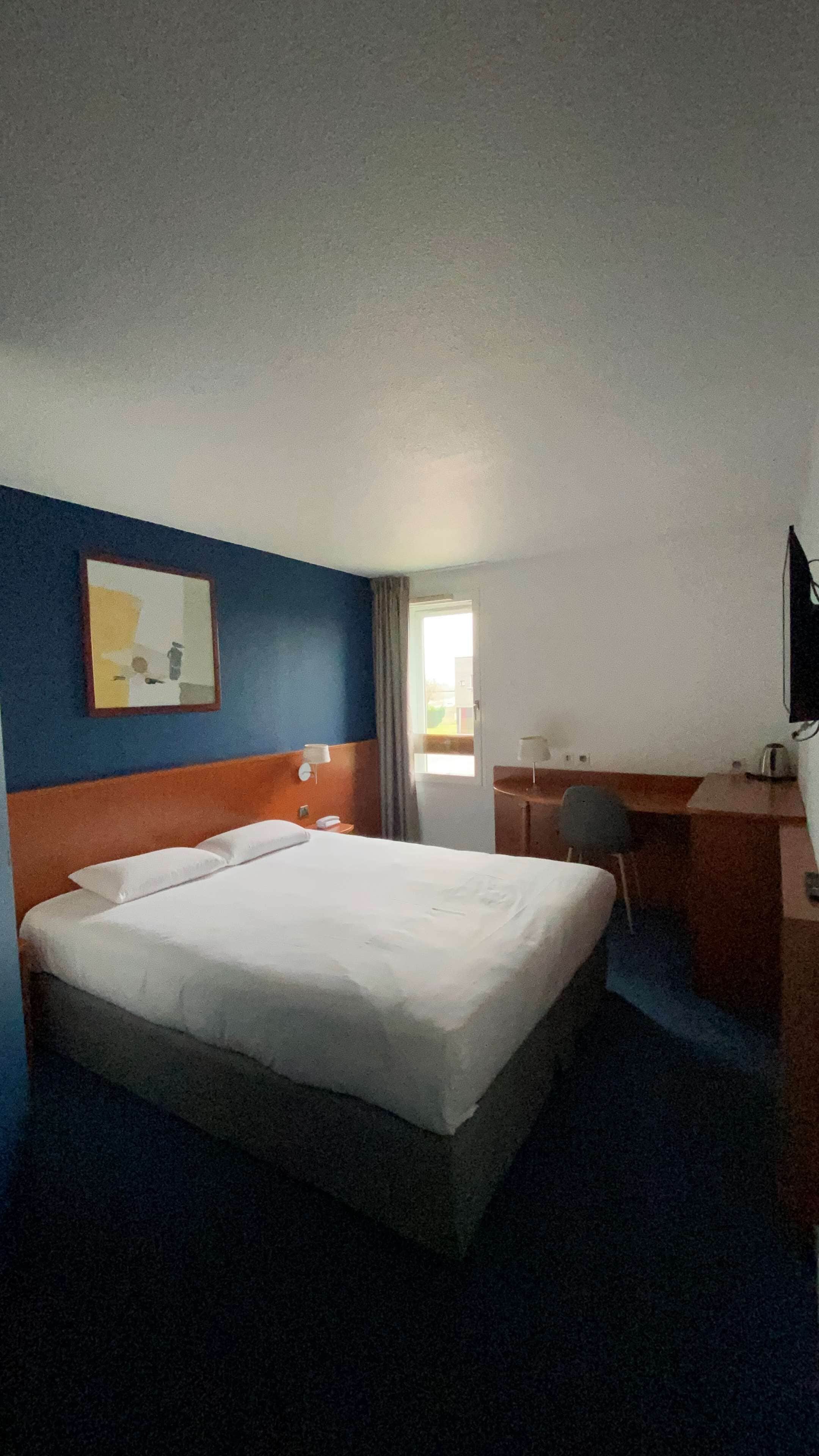 A hotel room with a bed, a desk, a chair, a television, and a window.