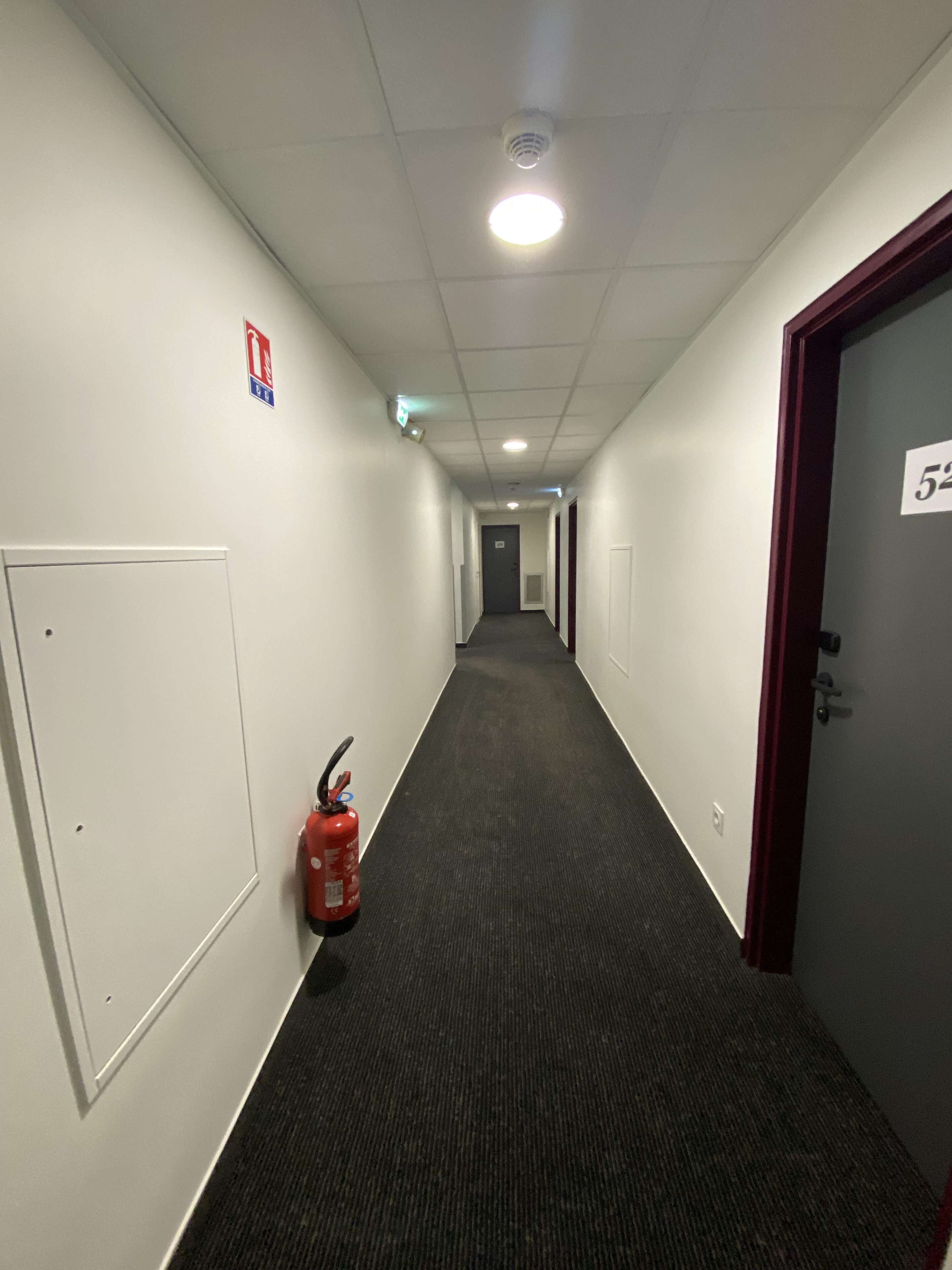 A hallway with a fire extinguisher, a fire alarm, and a door with the number 52.