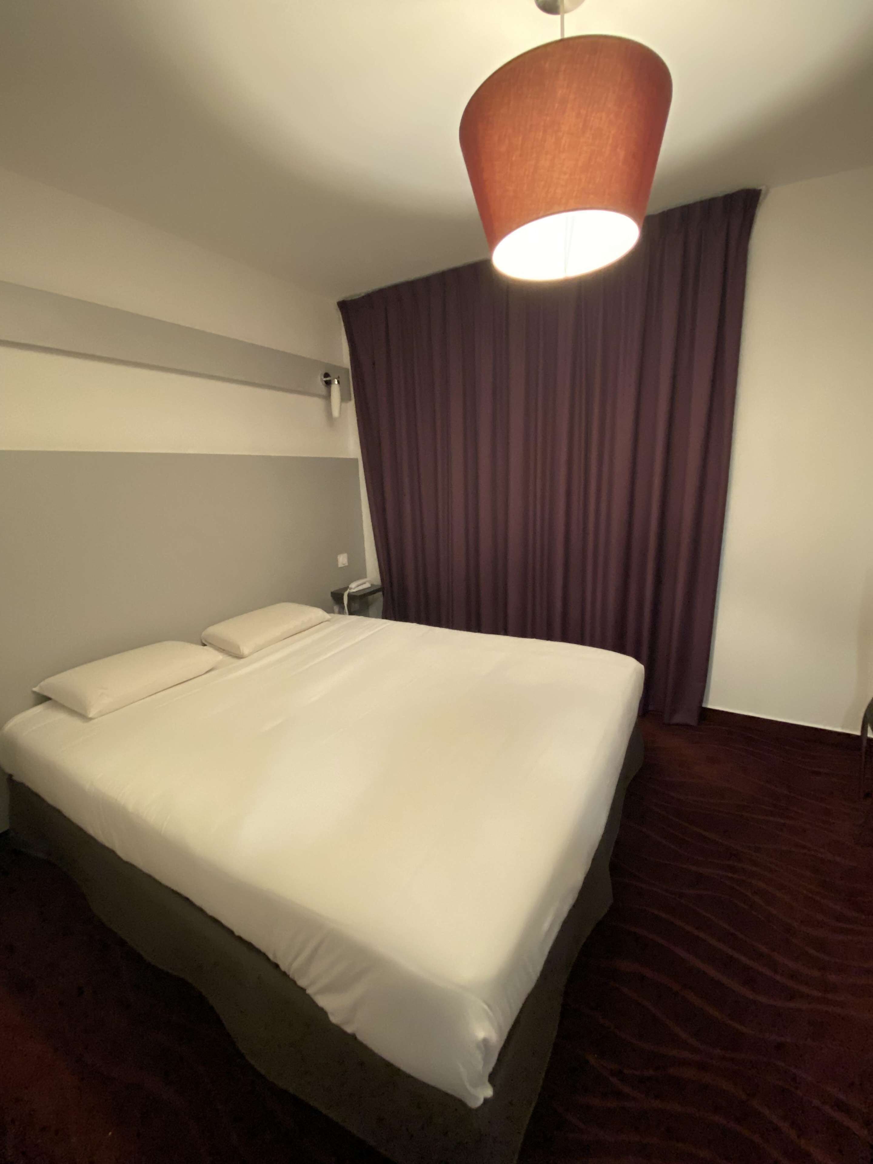 Ein Hotelzimmer mit einem großen Bett, einem Nachttisch, einer Lampe und dunklen Vorhängen.
