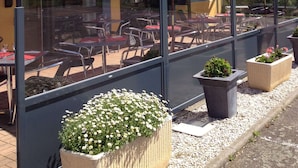 Een restaurant met terras, rode parasols en potplanten.