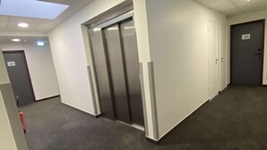 Een gang met een moderne lift, een brandblusser en een deur met het nummer 49.