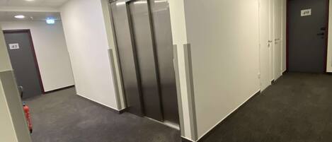 A corridor with a modern elevator, a fire extinguisher, and a door marked with the number 49.