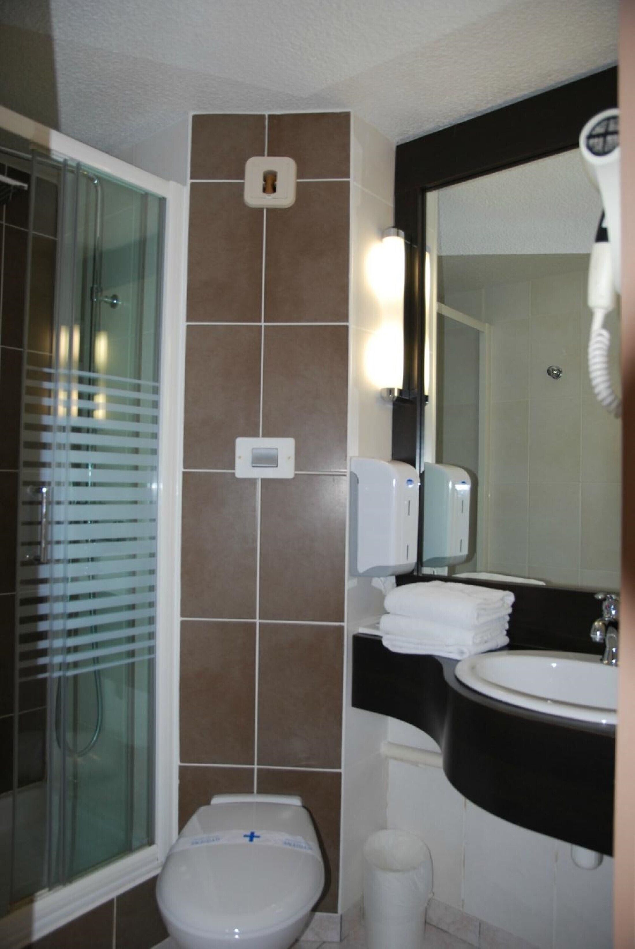 Un baño con cabina de ducha de vidrio, inodoro, lavamanos con espejo y secamanos.