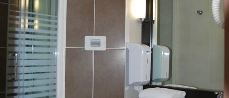 Un baño con cabina de ducha de vidrio, inodoro, lavamanos con espejo y secamanos.