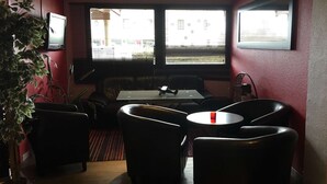 Een kamer met een tafel, stoelen, een kamerplant en een raam met jaloezieën.