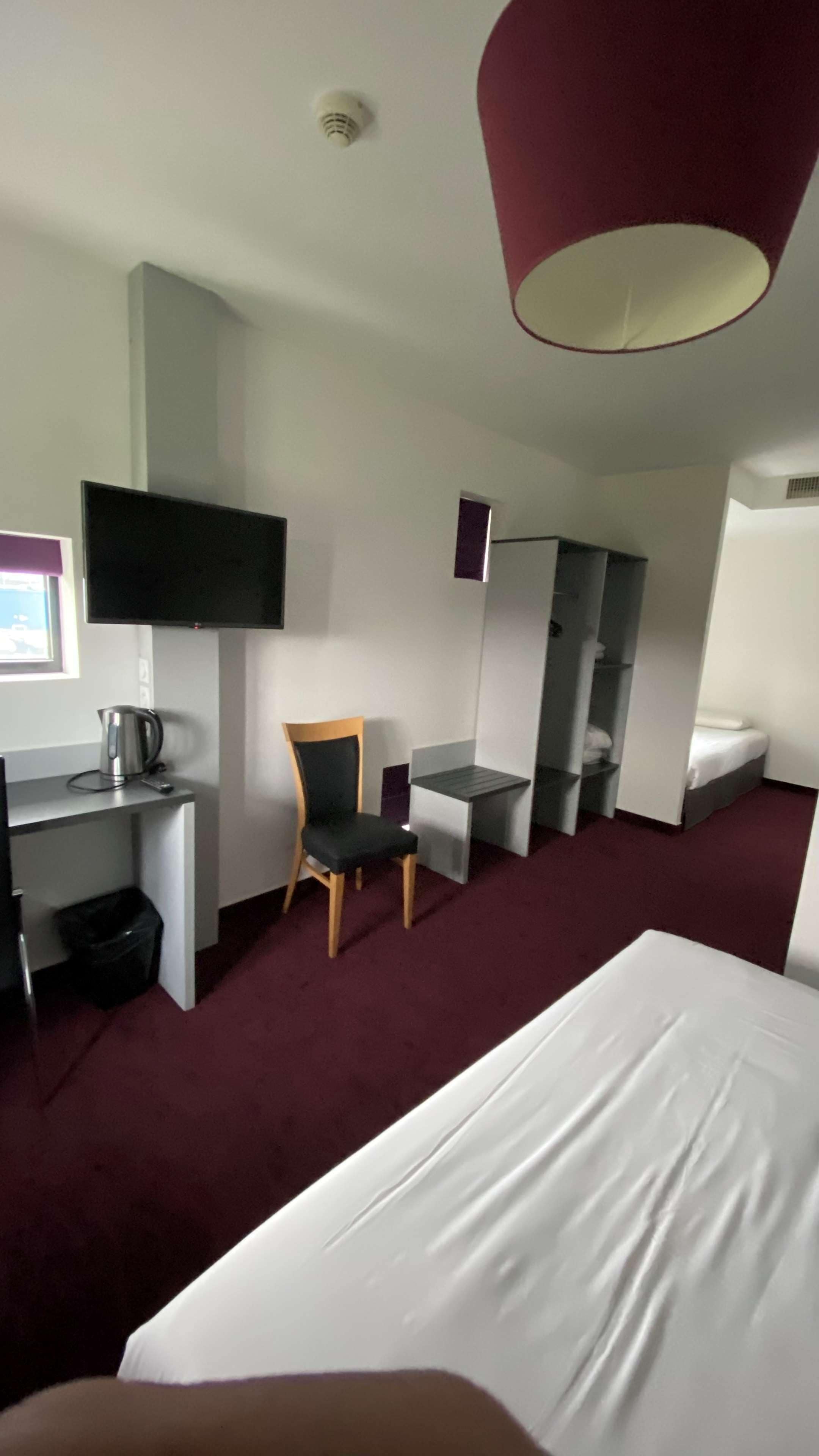 Habitación de hotel con cama, escritorio con silla, televisor, espejo y una pared de acento roja.