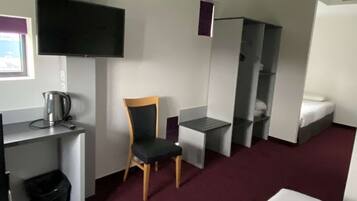 A hotel room with a bed, a desk with a chair, a television, a mirror, and a red accent wall.