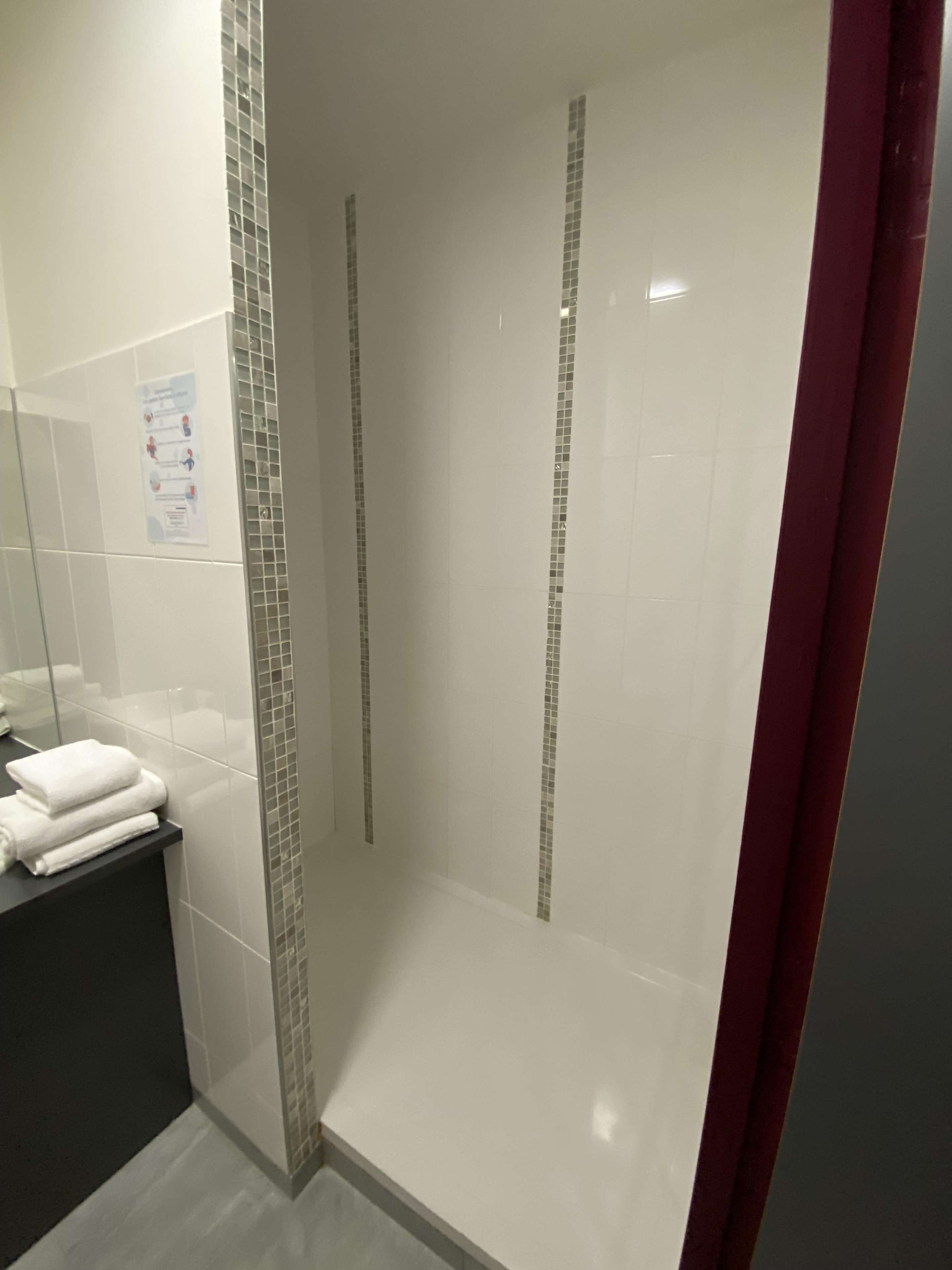 A bathroom with a tiled shower wall, a mirror, and a black countertop with folded towels.