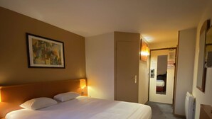 Een hotelkamer met een groot bed, nachtkastje, wandlamp en een lijst met een afbeelding.