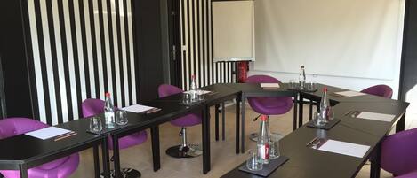 A conference room with a long table, purple chairs, and a white screen.