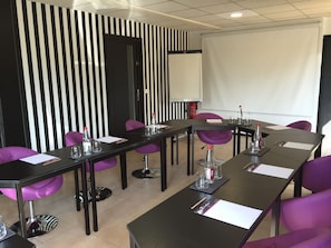 A conference room with a long table, purple chairs, and a white screen.