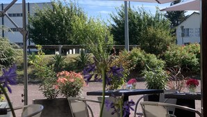 An outdoor patio area with a table and chairs, a large umbrella, and various potted plants.
