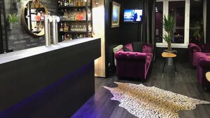 A bar area with a counter, shelves of bottles, a television, and purple seating.