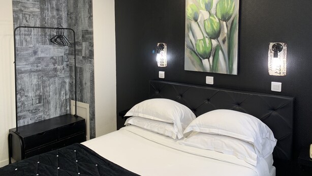 A bedroom with a black headboard, white bedding, a wall-mounted painting of green leaves, and a black wardrobe.