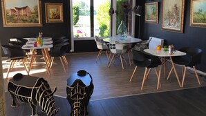 A dining area with tables and chairs, artwork on the walls, and a view through the glass door.