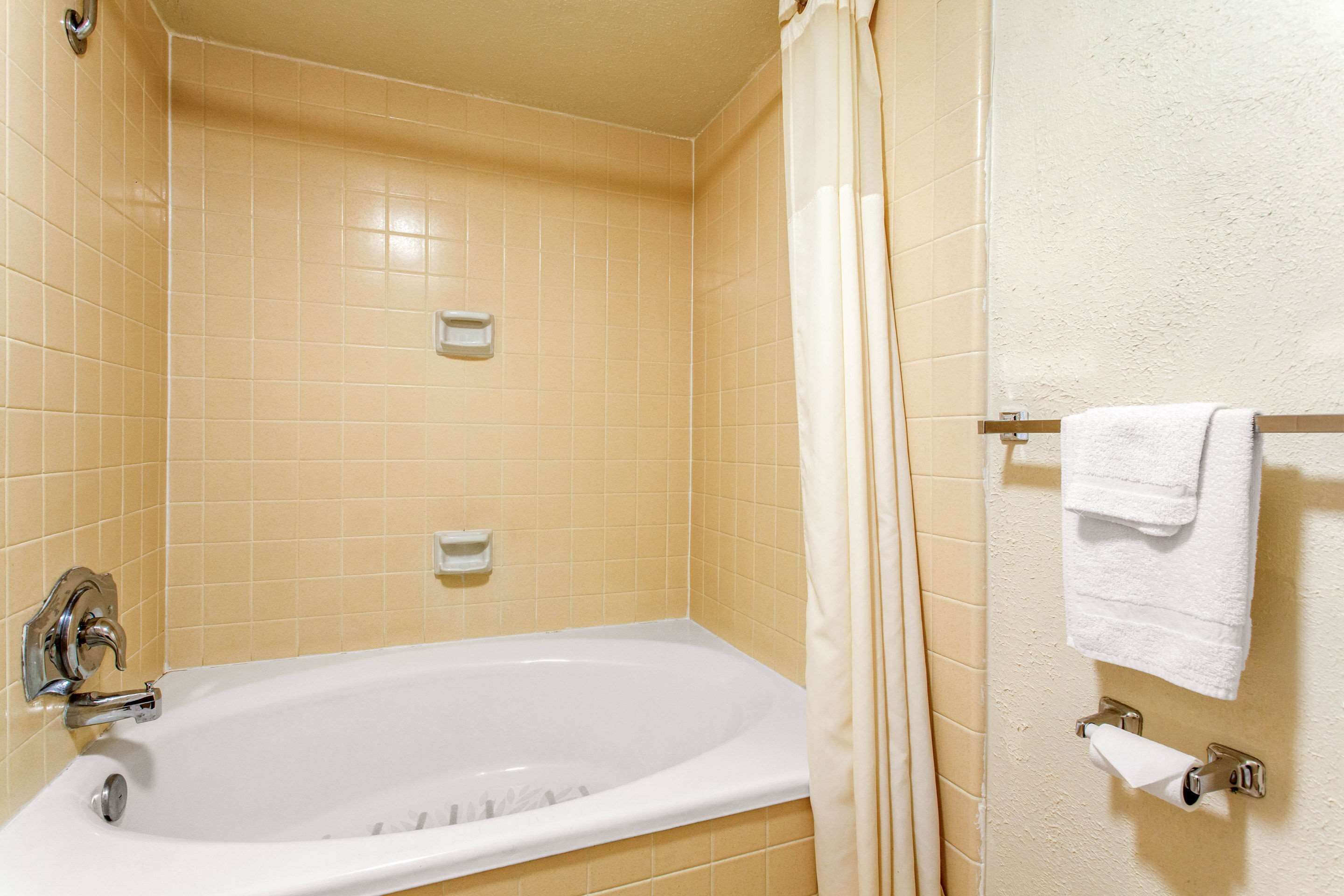 Un bagno con una vasca, un portasciugamani con un asciugamano bianco e un porta carta igienica.