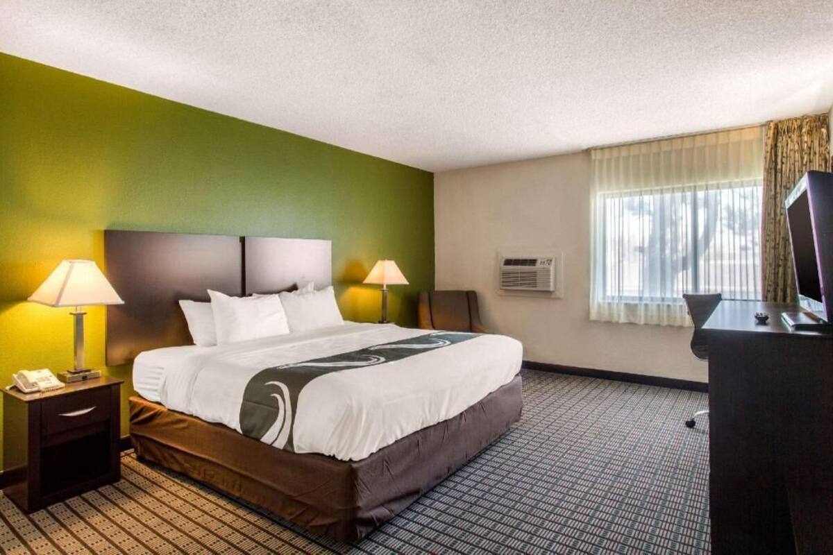 A hotel room with a bed, two bedside lamps, a desk with a television, and a window with curtains.