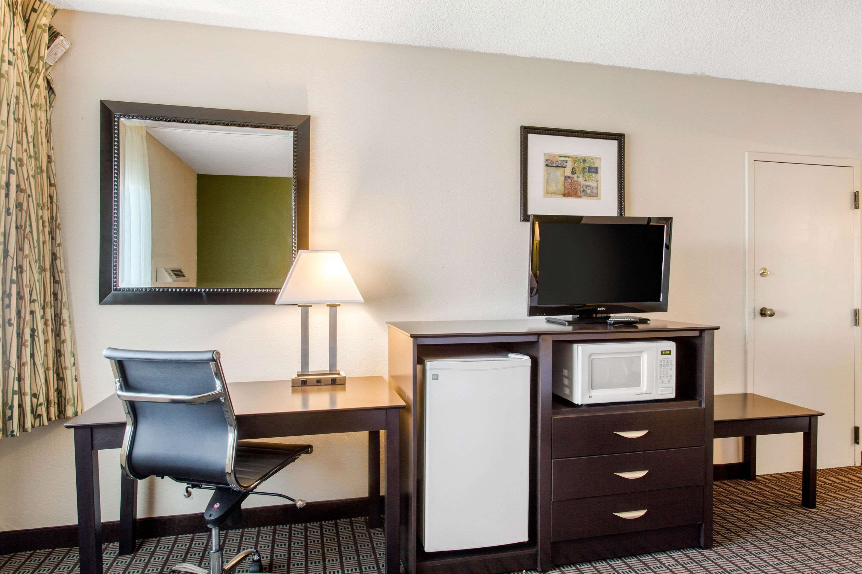 Habitación de hotel con escritorio, silla, televisor, microondas y refrigerador.