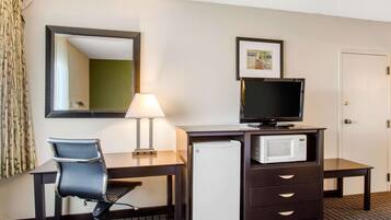 Habitación de hotel con escritorio, silla, televisor, microondas y refrigerador.