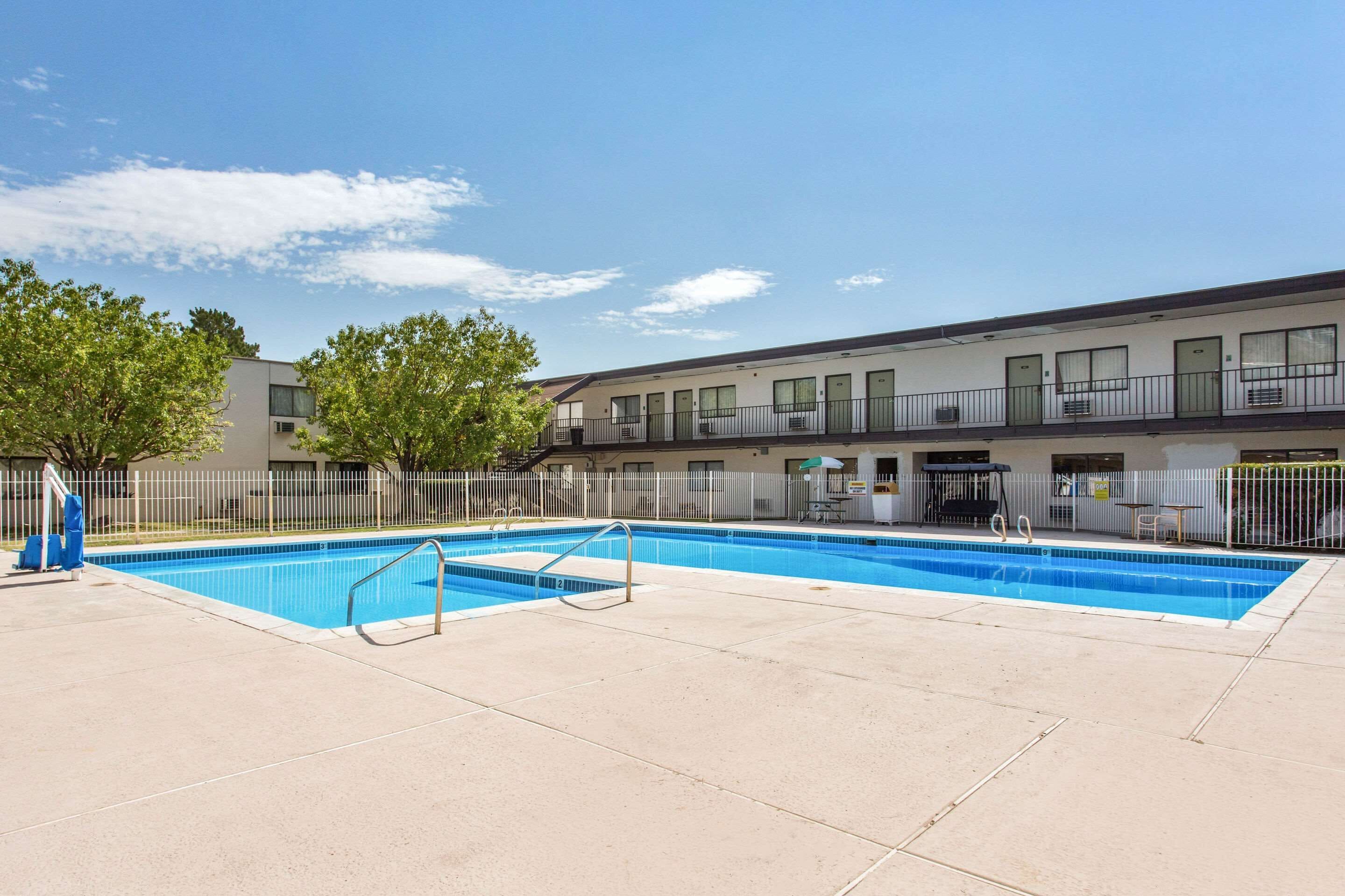 A rectangular outdoor swimming pool with a metal ladder, surrounded by a fence, and adjacent to a building with multiple windows and balconies.