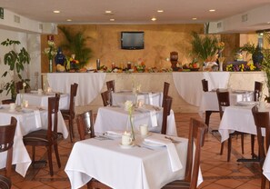 Un restaurante con varias mesas dispuestas para comer, sillas y un televisor montado en la pared.