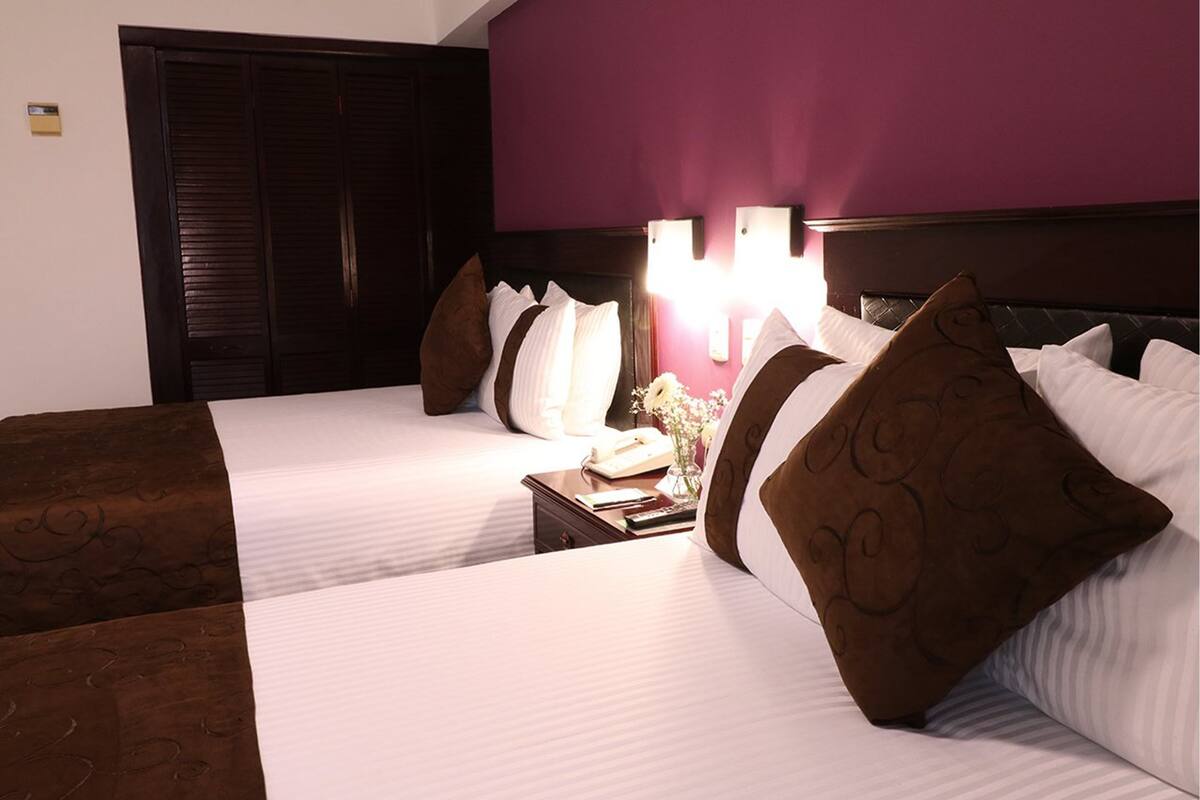 A hotel room with two beds, a nightstand with a lamp, and a large wardrobe.