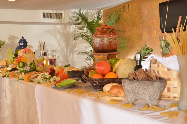 Une table garnie de divers fruits, légumes et pains, décorée de fleurs et d’un grand pot en argile.