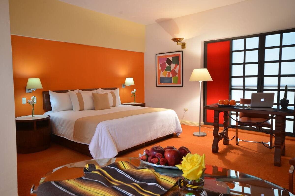 A hotel room with a bed, a desk, a laptop, and a fruit bowl.