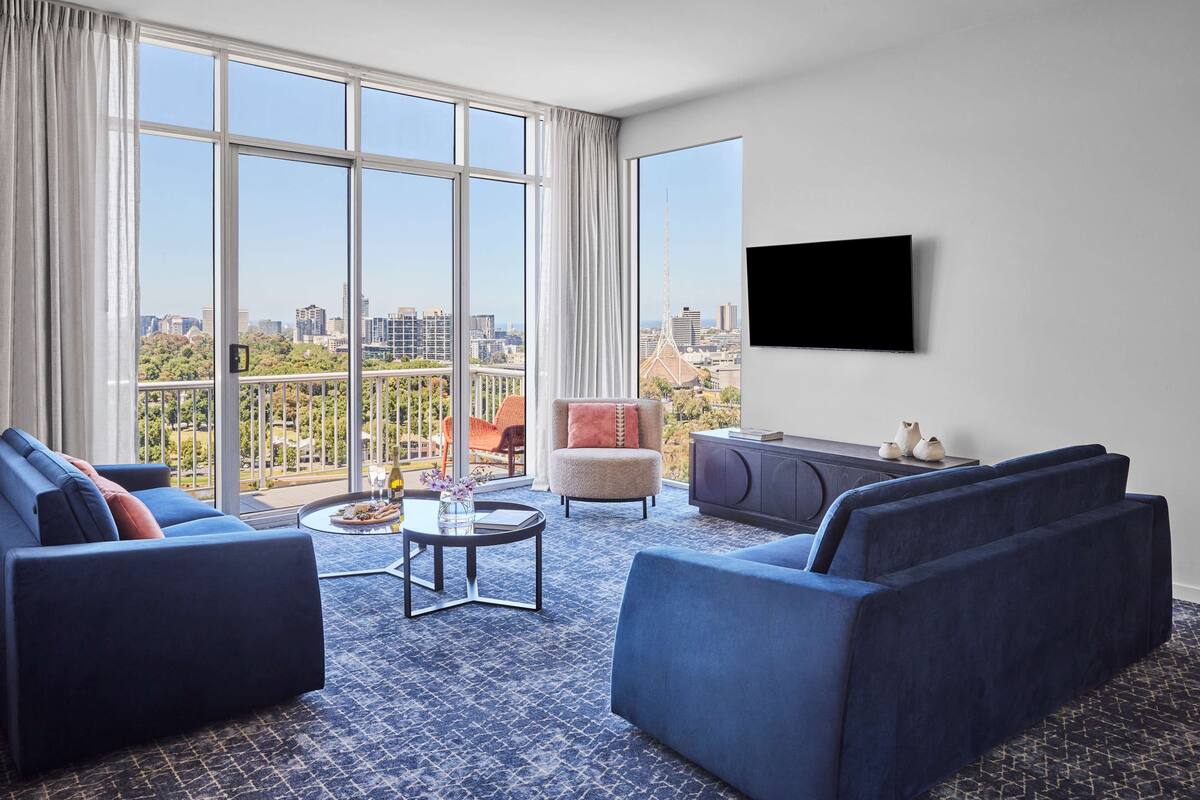 A modern living room with a city view, featuring a sofa, armchair, and a coffee table.