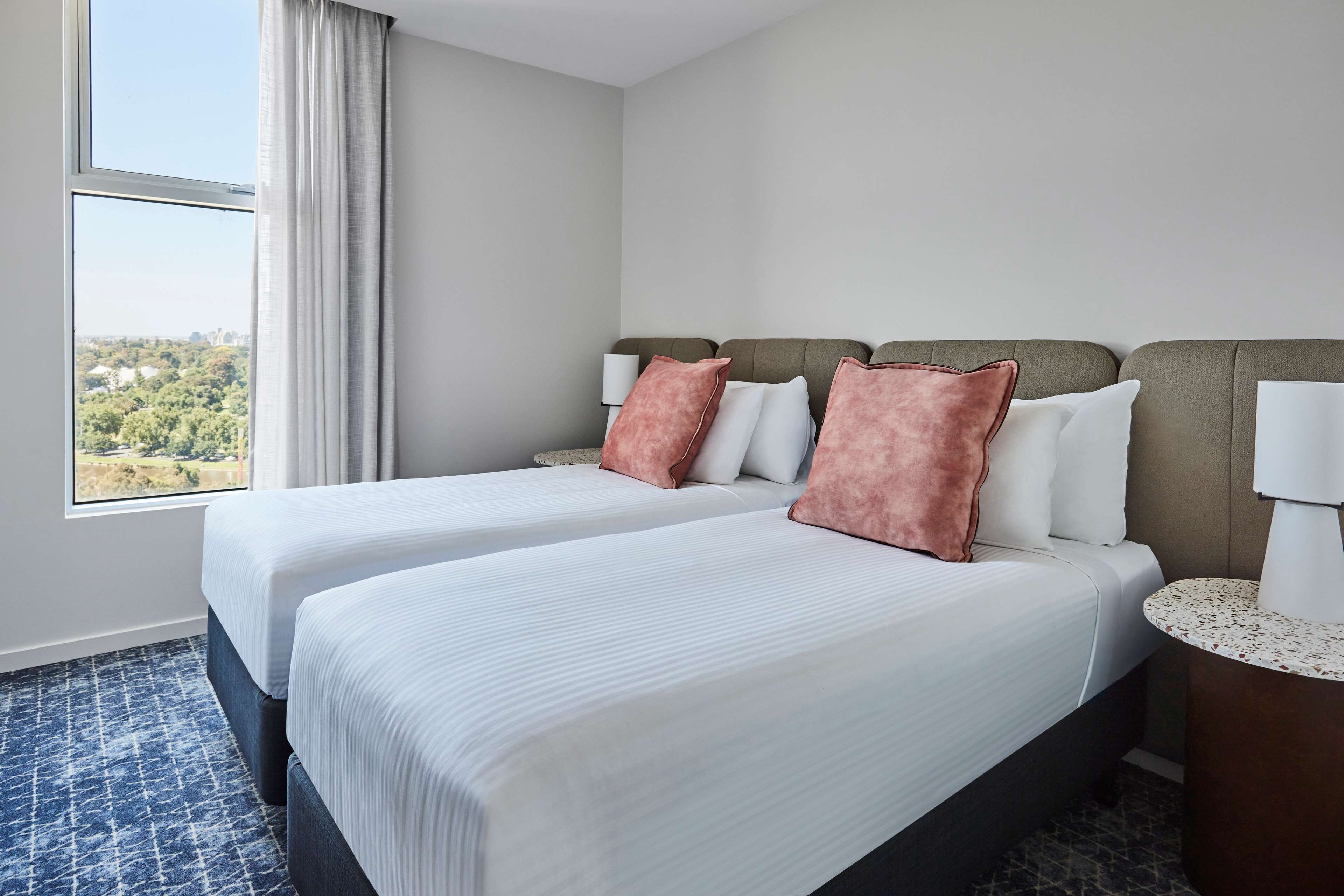 Quarto de hotel com duas camas, uma mesinha redonda e vista para a paisagem urbana.