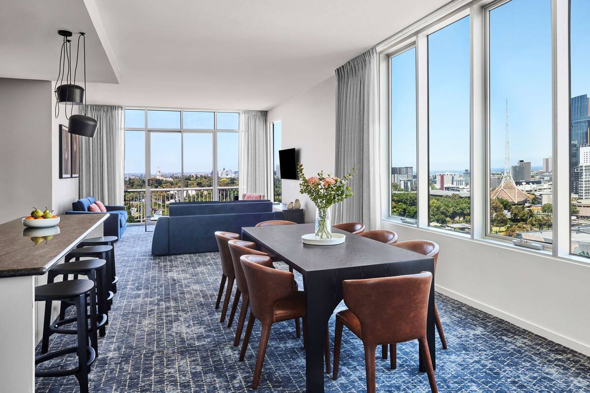 A modern hotel room with a dining area, large windows with city views, and a seating area with a view.
