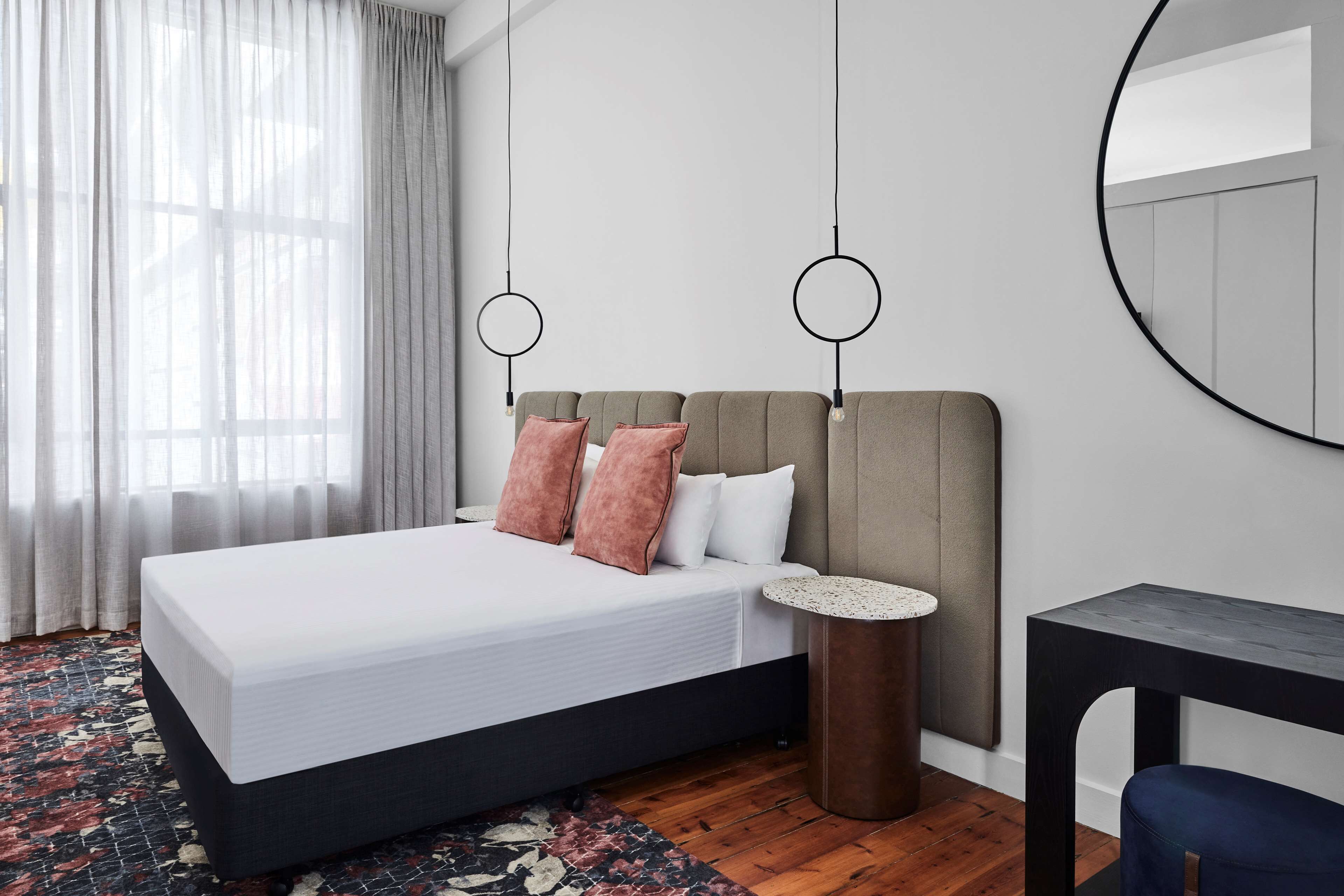 Une chambre à coucher moderne avec un grand lit, une table de chevet ronde, une petite table ronde et un miroir au mur.
