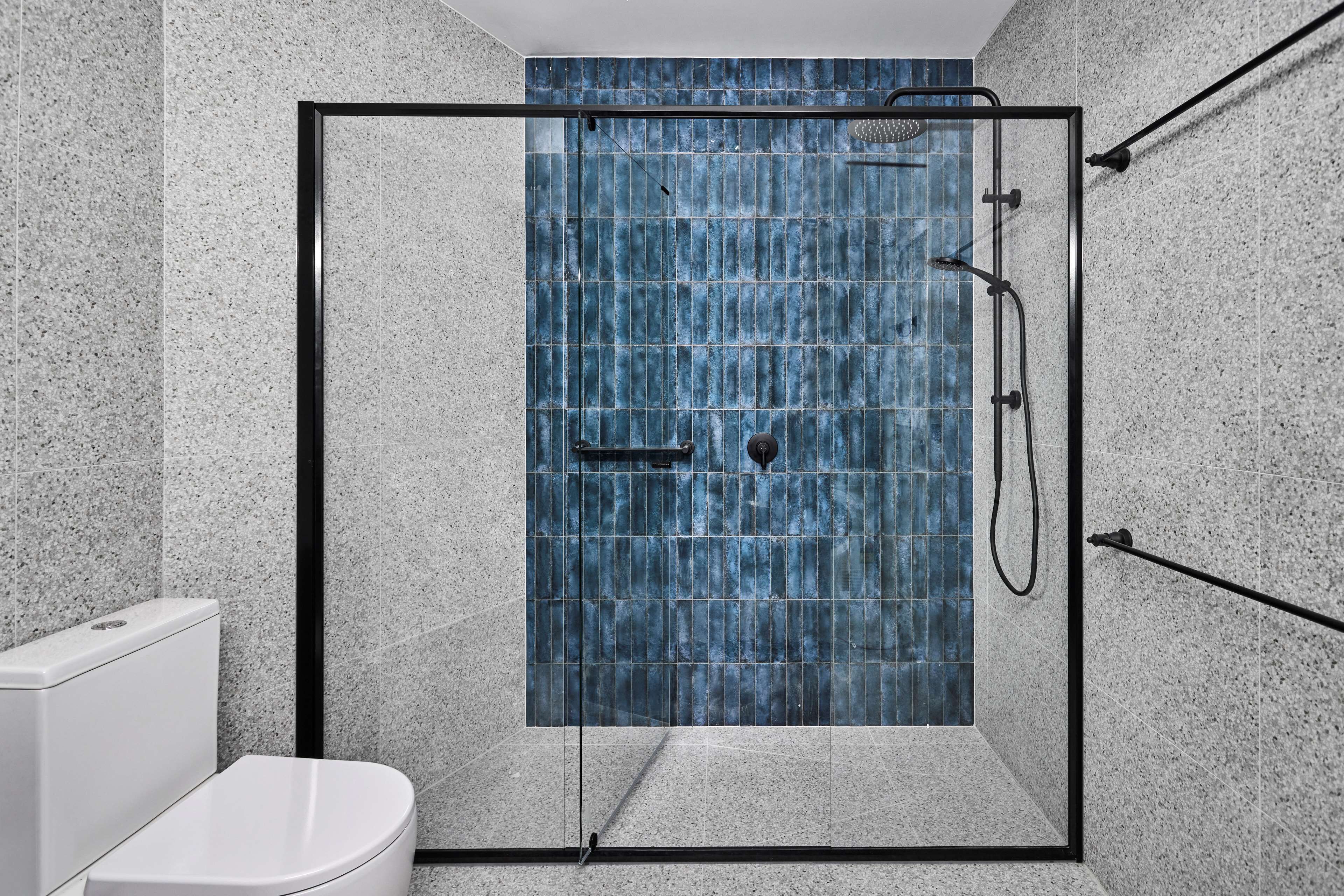 Une salle de bain moderne avec une douche à parois de verre, des toilettes blanches et un mur recouvert de carreaux.