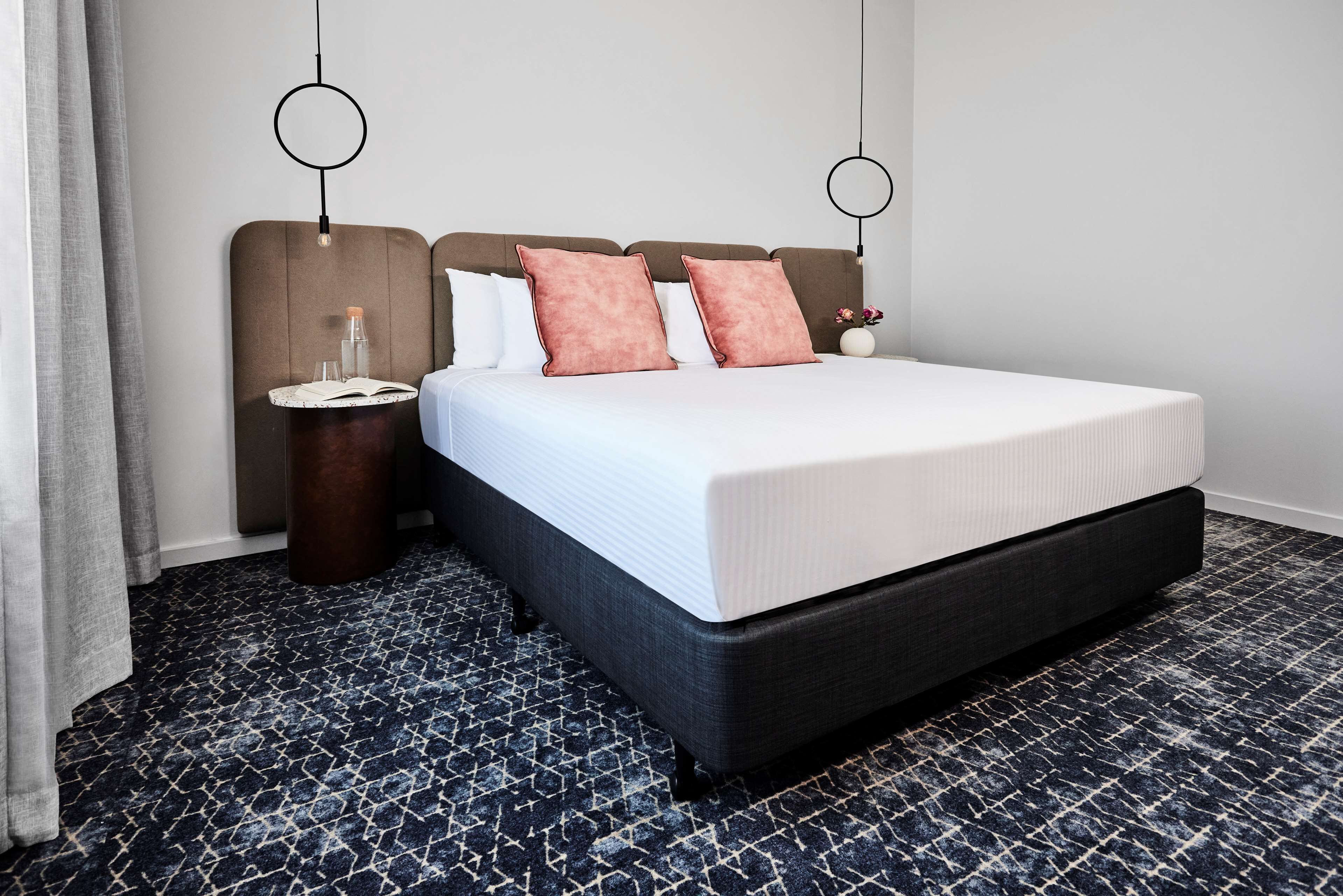 Ein Hotelzimmer mit einem großen Bett, einem runden Beistelltisch, einem Nachttisch und einer Wandlampe.