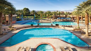Un área de piscina en un complejo turístico con varias piscinas, sillas de descanso y palmeras.