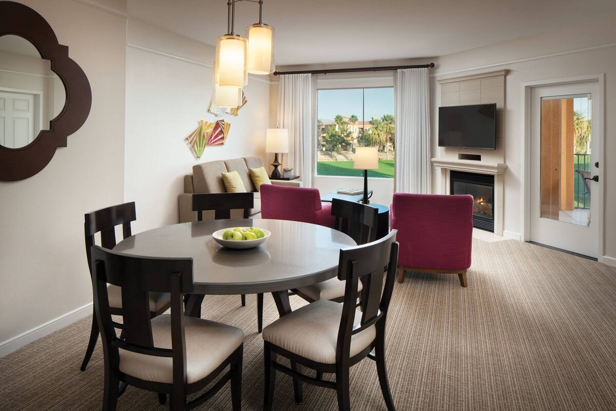 A hotel room with a dining area, a sofa, a TV, and a fireplace.