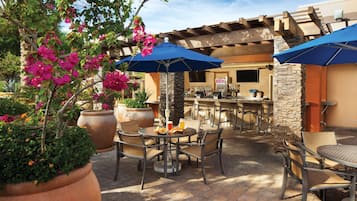 An outdoor patio with round tables and chairs, blue umbrellas, and potted plants.