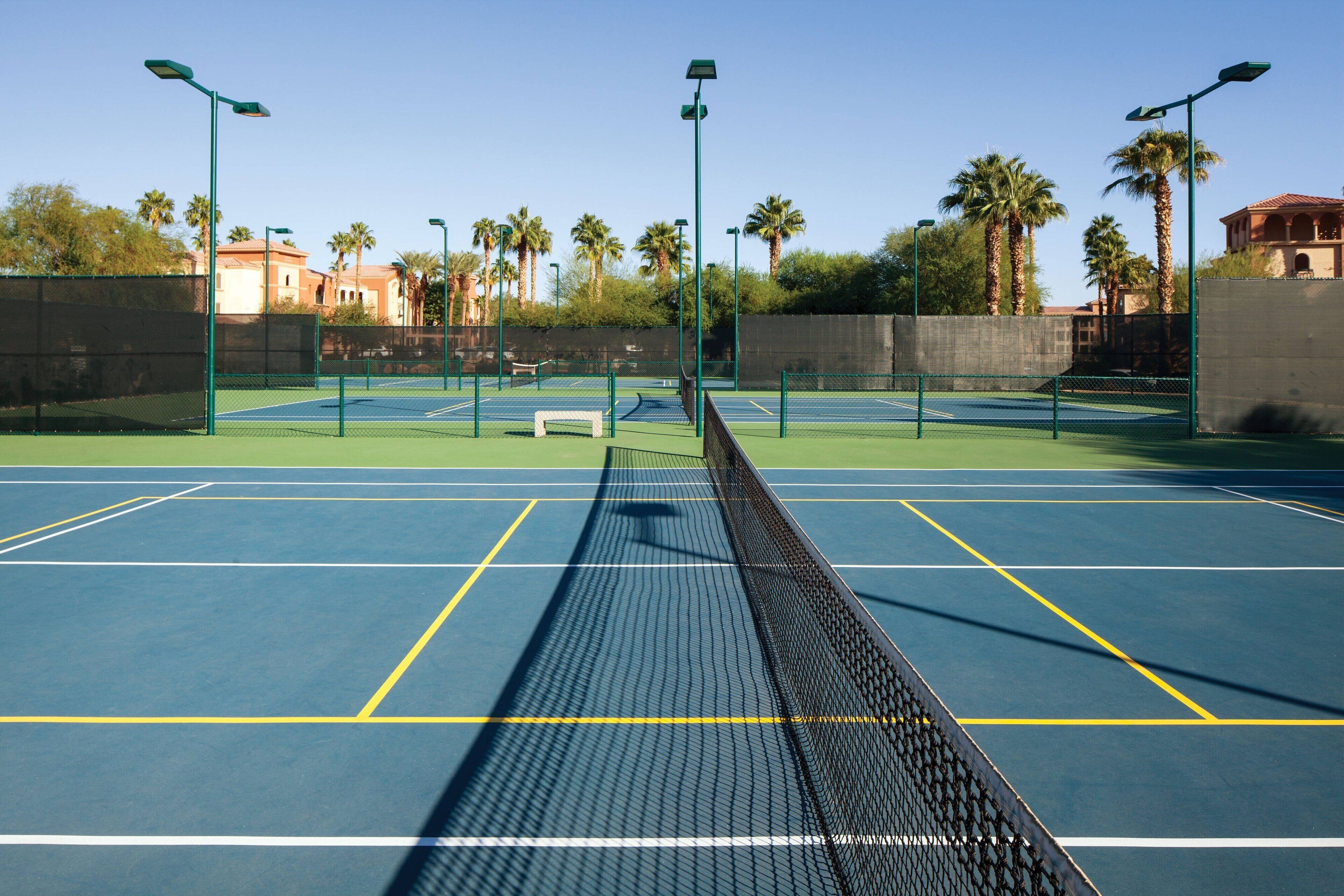 Un court de tennis avec un filet, entouré de palmiers et éclairé par des lampadaires.