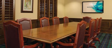 A conference room with a long wooden table, six chairs, a screen displaying "WELCOME", and a plaid carpet.
