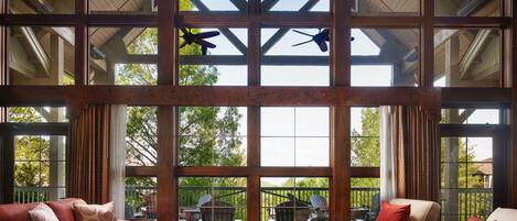 A spacious room with large windows, wooden beams, and two ceiling fans.