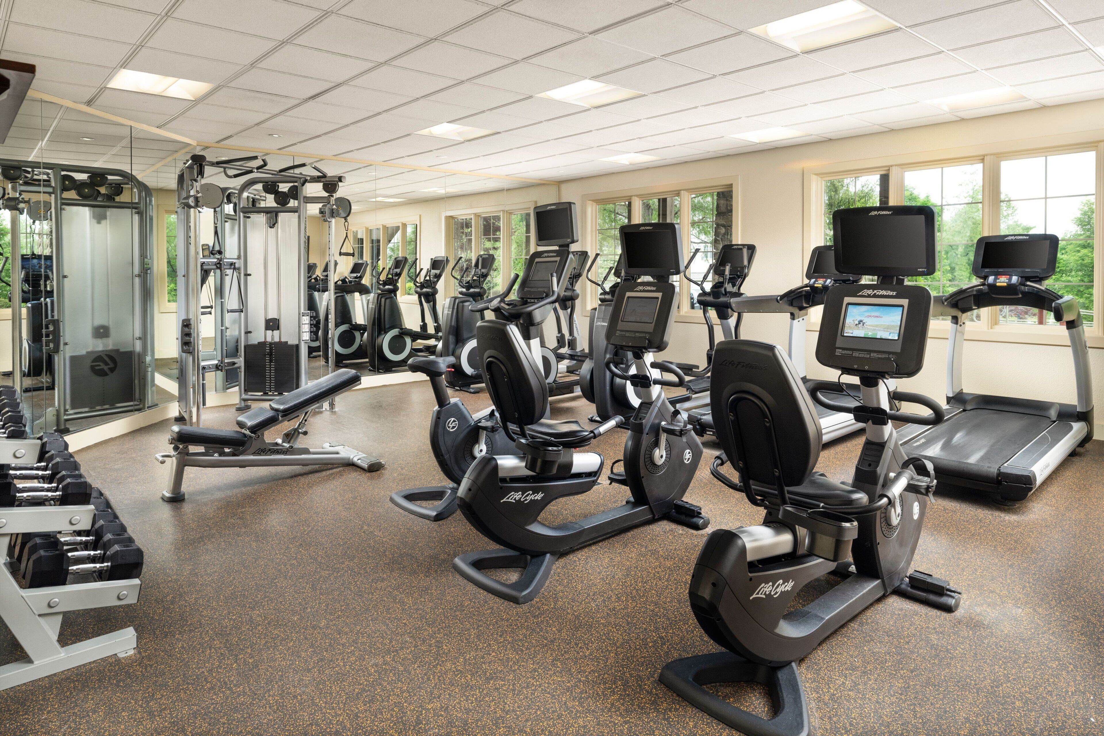 A gym with multiple cardio machines, weight machines, and dumbbells.