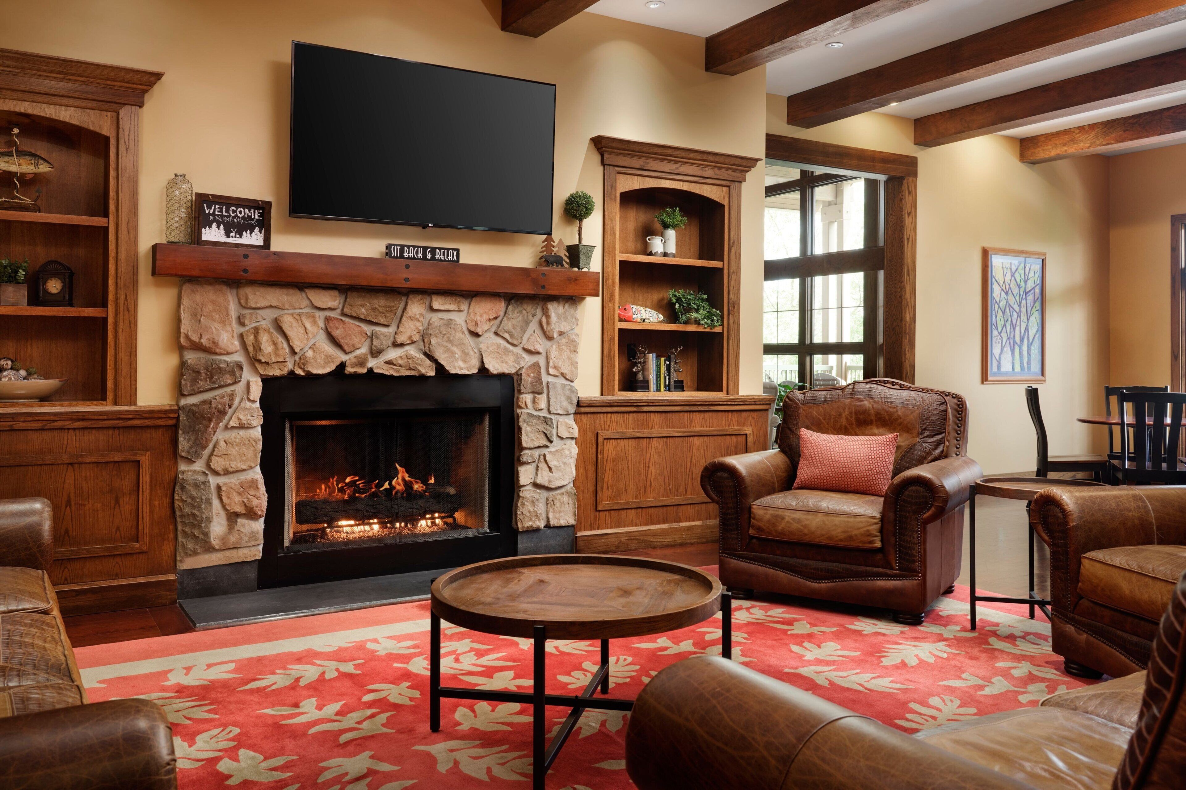 A cozy living room with a stone fireplace, leather furniture, and a flat-screen TV mounted above the fireplace.